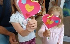 Dwie dziewczynki trzymają w rękach laurki dla mamy w kształcie serca.