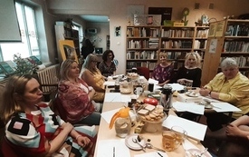 Grupa kobiet w średnim wieku siedzi wok&oacute;ł zastawionego stołu