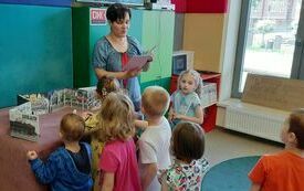 Kobieta opowiada coś dzieciom, kt&oacute;re stoją i patrzą. 