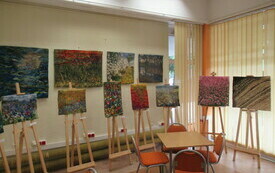 Kolorowe gobeliny wiszą na ścianie oraz leżą na sztalugach