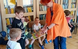 Dzieci oglądają książkę, którą trzyma w ręku kobieta prowadząca spotkanie.