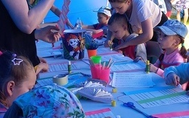 Przy stolikach grupa dzieci biorących udział w warsztatach tworzenia wachlarzy z papieru.
