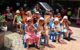 Grupa dzieci siedzi na kolorowych krzesełkach