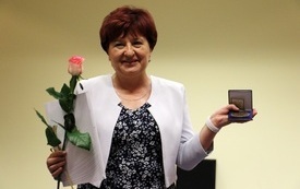 Starsza kobieta pozuje do zdjęcia z medalem i kwiatami