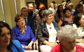 Grupa dorosłych, elagancko ubranych osób siedzi na krzesłach