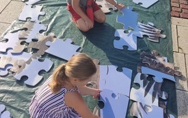 Dziewczynka i chłopiec układają na ziemi wielkie puzzle ze zwierzętami