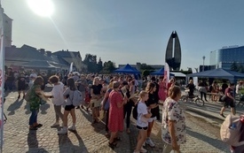 Grupa starszych i młodszych osób stoi na brukowanym placu