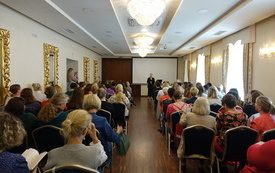Po dw&oacute;ch stronach sali konferencyjnej rzędy krzeseł, na kt&oacute;rych siedzą kobiety.  