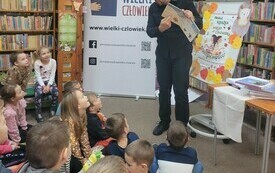 Grupa dzieci zwrócona w kierunku prowadzącego spotkanie mężczyzny.