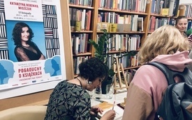 Gość spotkania, kobieta w średnim wieku podczas rozdawania autografów. Obok kobieta z plecakiem.
