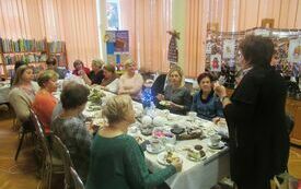 Uczestnicy warsztat&oacute;w, kobiety w r&oacute;żnym wieku, siedzą wok&oacute;ł stołu i wykonują świąteczne anioły