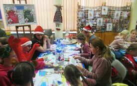 Grupa dzieci wraz z opiekunami podczas wykonywania aniołk&oacute;w. Wok&oacute;ł dekoracje świąteczne.