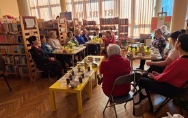 Na stoliku bufet z herbatami i ziołami. Kobiety uczestniczące w spotkaniu.