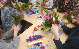 Na stole materiały do stworzenia palm. bibuła, kwiaty z papieru, bukszpan, nożyczki, sznurki. 