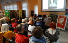 Grupa starszych os&oacute;b siedzi przed ekranem z wyświetloną prezentacją na temat malarstwa