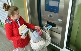 Kobieta pokazuje grupie dzieci jak zwr&oacute;cić książkę przy użyciu wrzutni. 