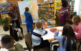Chłopiec wskazuje coś na mapie. Obok grupa dzieci siedzi przy stoliku.