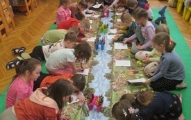 Grupa dzieci siedzi na dywanie i koloruje obrazki.