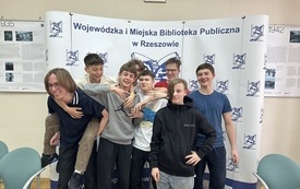 Grupa chłopaków na tle ścianki z logo biblioteki.