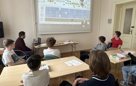 Grupa młodzieży bierze udział w grze planszowej, którą prowadzi bibliotekarz.