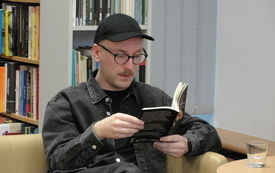 Mężczyzna w czapce z daszkiem i okulrach, trzyma w ręku książkę. 