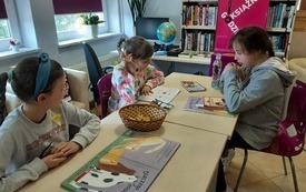 Trzy dziewczynki siedzą przy stole i przeglądają książki. 