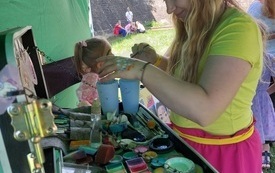 Dziewczyna zajmuje się malowaniem twarzy dzieciom. 