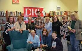 Grupa ludzi stoi obok siebie, w środku Jakub Małecki. W tle logo Dyskusyjnych Klub&oacute;w Książki.