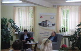 Bibliotekarka z Ks. Kazimierz Sowa siedzą na fotelach i rozmawiają.