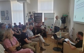 Dwa fotele, stolik, prezentacja na ścianie oraz krzesła z uczestnikami wykładu.