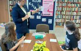 Kobieta pokazuje dzieciom kartkę kolorowego papieru.