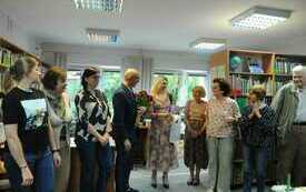 Grupa ludzi stoi, wójt gminy Komańcza trzyma bukiet róż. W tle regały z książkami.