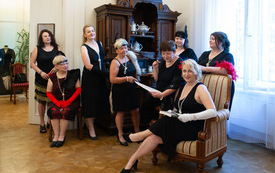 Grupa kobiet w sukienkach pozuje do zdjęcia, w tle meble.