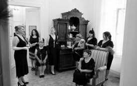 Grupa kobiet w wieczorowych sukienkach, w tle drewniany kredens.