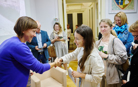 Dwie kobiety uściskają sobie dłoń. Wokół zebrana publiczność.