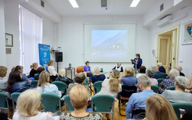 Kobieta w marynarce przemawia do zebranych w sali osób.