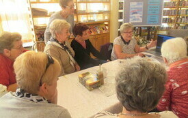 Kilka kobiet siedzących przy stole i oglądających zdjęcia na laptopie.