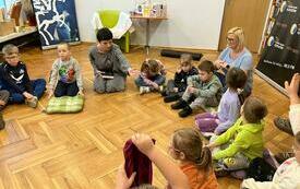 Grupa dzieci w k&oacute;łku na podłodze z dwiema kobietami.
