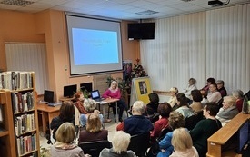 Uczestnicy spotkania zebrani w bibliotece na prelekcji. 