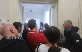 Ludzie zebrani tłumnie w korytarzu, pr&oacute;bują wejść do sali. 