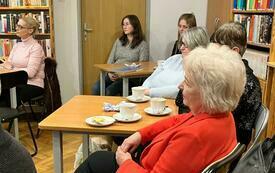 Grupa osób przy siedzaca przy stolikach.