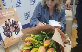 Bukiet kwiatów oraz dziennikarka podpisująca swoje książki.