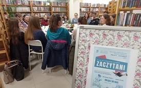 biblioteczna sala , w kt&oacute;rej przy stole siedzą młodzi ludzie