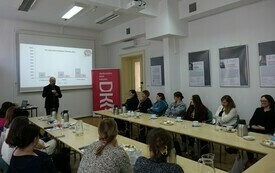 Sala szkoleniowa wypełniona uczestnikami oglądającymi prezentację na ekranie