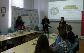 Widok sali szkoleniowej i prowadzącego, który stoi przy ekranie z prezentacją