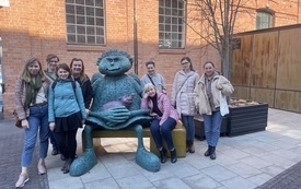 Grupa kobiet pozuje do zdjęcia przy rzeźbie anioła trzymającego w objęciach świnkę.