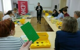 Klocek Lego, w tle bibliotekarki. 