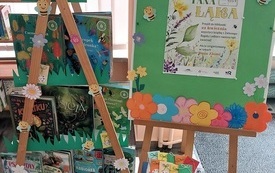 Regał z książkami i sztaluga z plakatem.