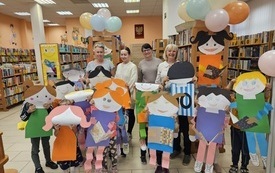 Cztery bibliotekarki z grupą dzieci trzymających postacie z książkami wycięte z papieru.