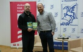Gość spotkania pozuje do wsp&oacute;lnego zdjęcia z mężczyzną trzymającym w ręku książki.